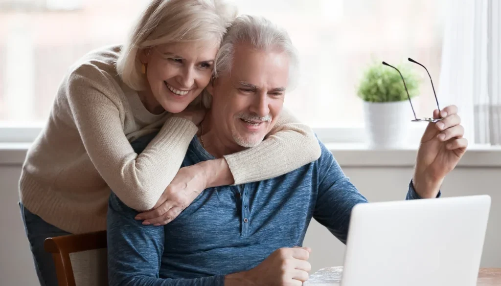 A retired couple looking at a laptop with smiles on their faces