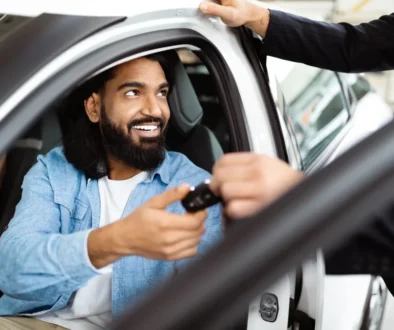 Smiling Man Receiving Car Keys From Salesperson at Vehicle Dealership