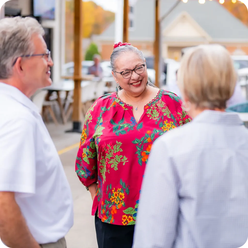 Three people chatting and smiling together at an outdoor social event.