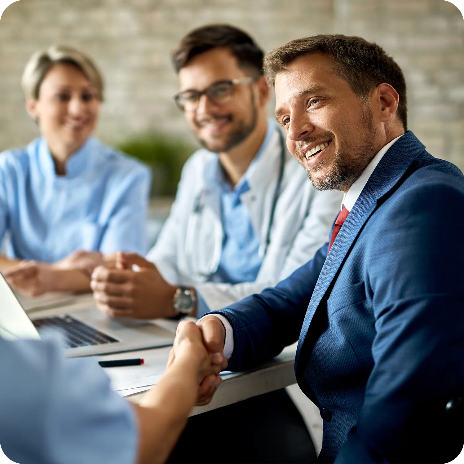Businessman shaking hands with a healthcare professional during a meeting with medical staff.