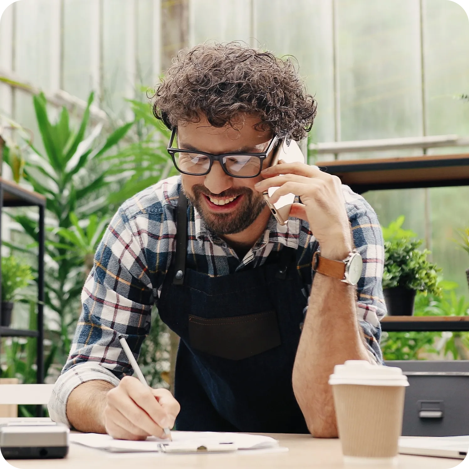 Smiling small business owner taking a phone call while writing at a desk.