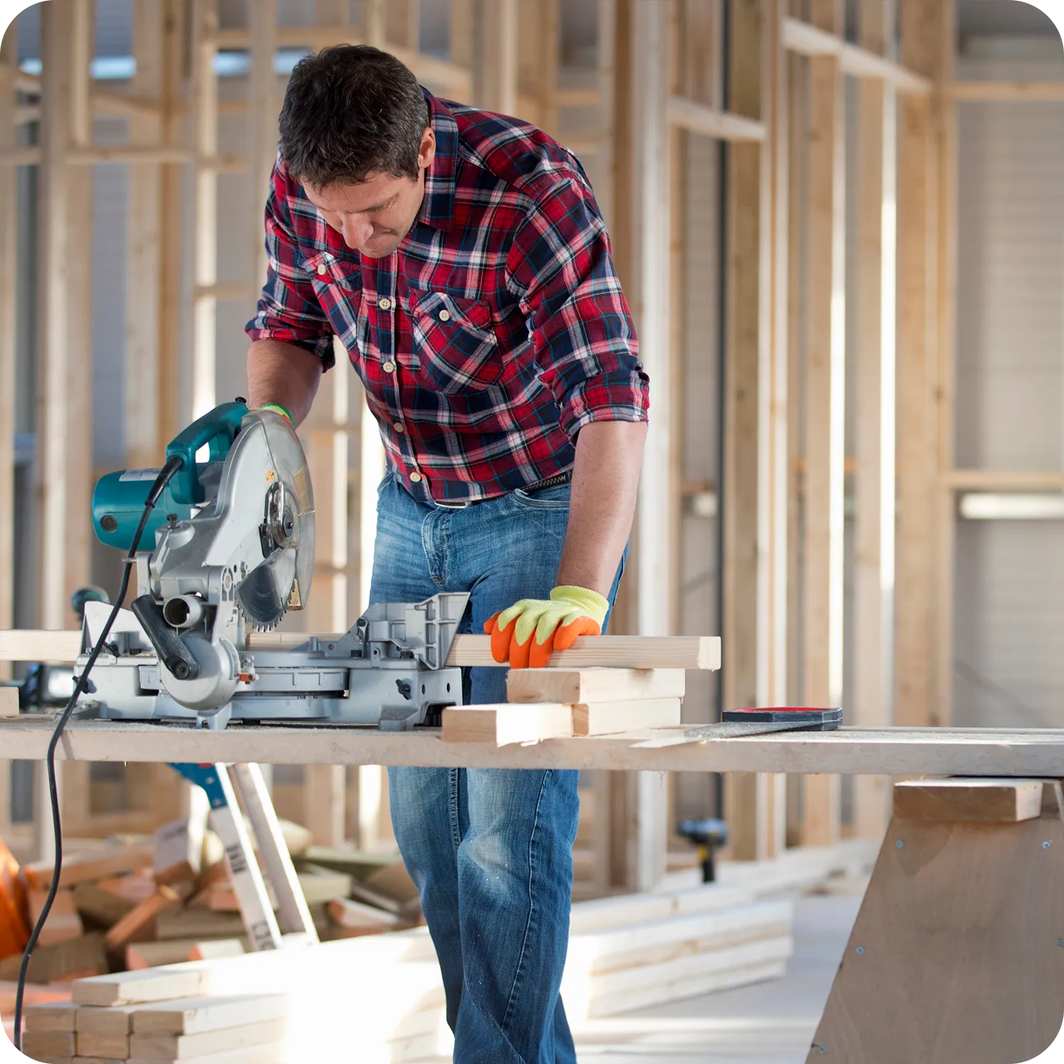 Carpenter cutting timber with a mitre saw inside a timber-framed building under construction.